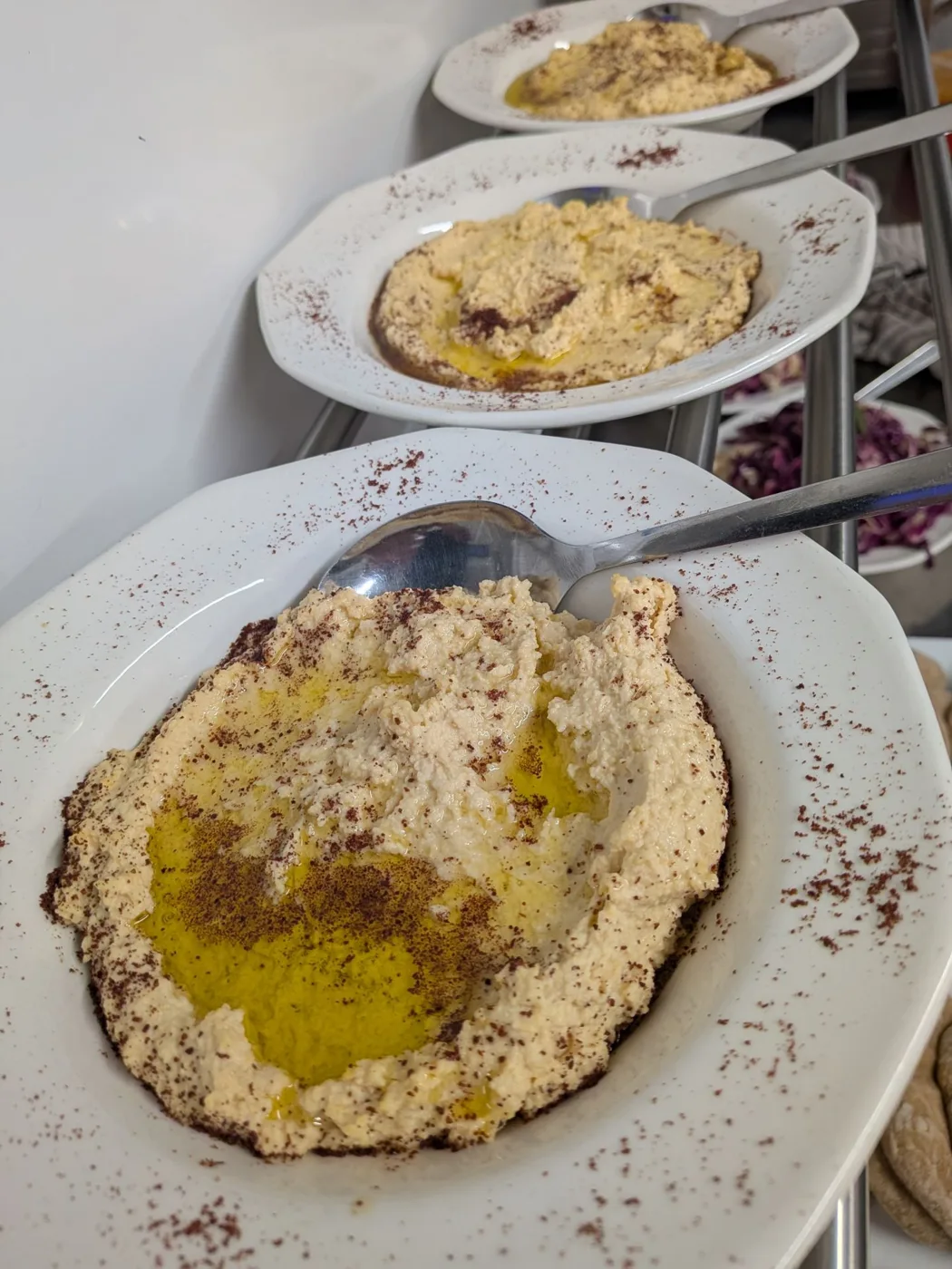 Three plates of hummus dusted with spice and drizzled with oil, with spoons